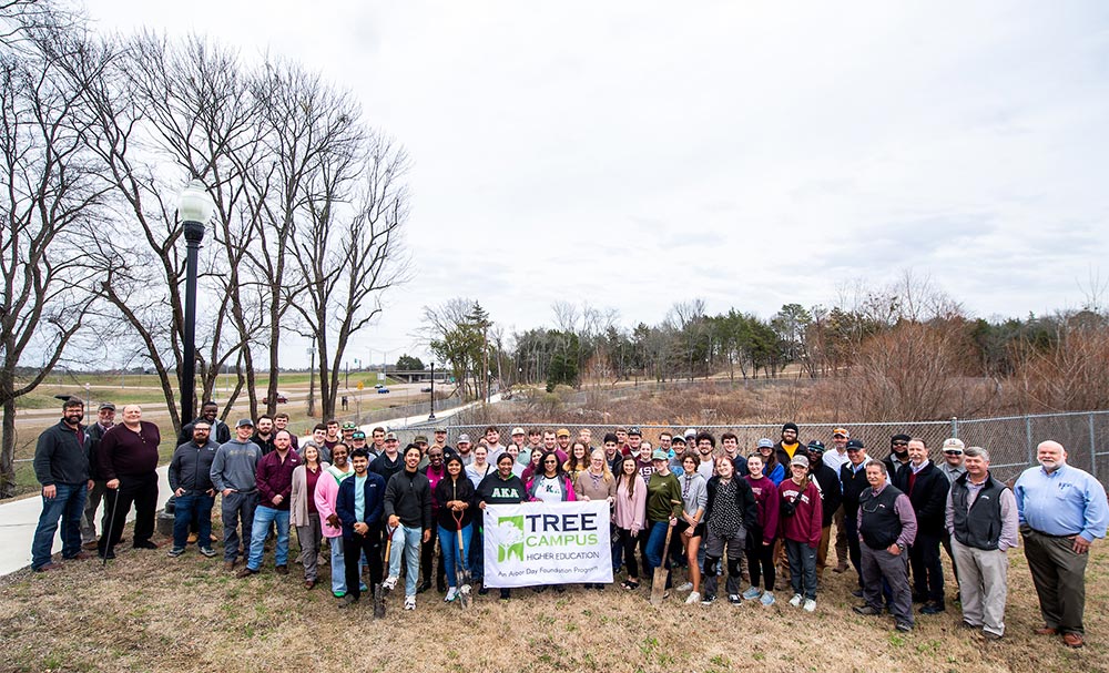 A large crowd of 爱爱直播 students, faculty and staff with a Tree Campus USA banner at the Arbor Day celebration